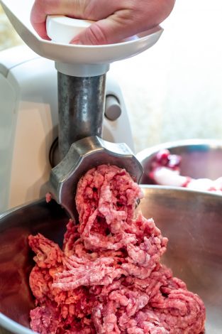 Process of meat grinding in the kitchen with mincing machine.